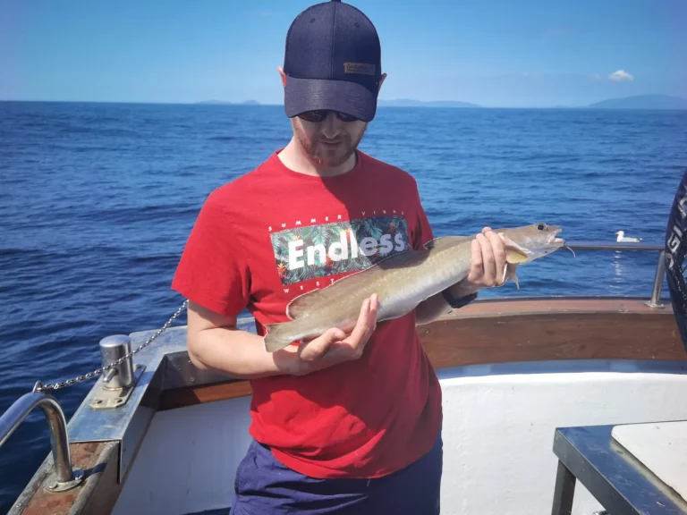 artem-kniaz-DqgMHzeio7g-unsplash Angler holding a fish on deck with the sea behind